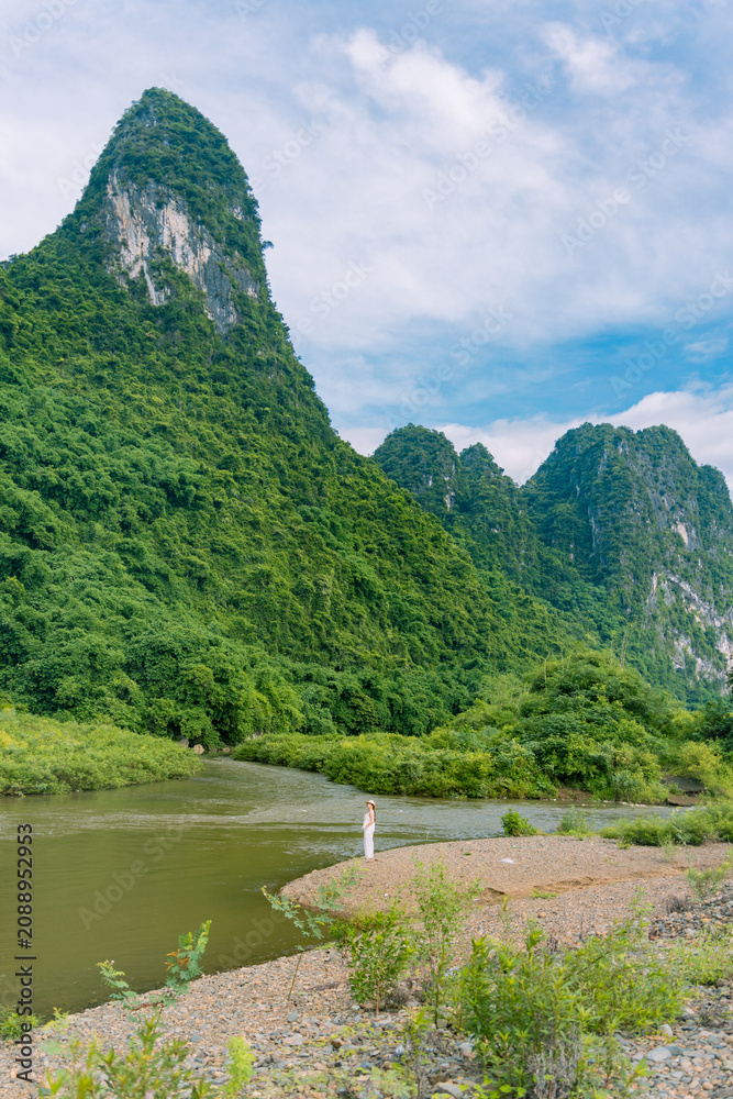 Fototapeta premium Woman in white outfit standing beside winding river, Ninh Binh, Vietnam