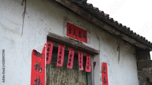 Weathered rural house with red Spring Festival couplets and blessings on doorway in Guangxi China. Traditional Chinese New Year decoration. Concept of festive culture, rural heritage, folk tradition