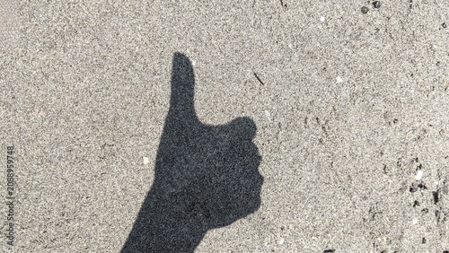 Thumb Up Hand Shadow on Beach Sand Background with Copy Space