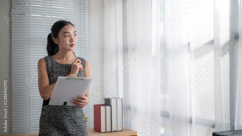 Young Woman Holding Pen and Notepad Looking Out Window in Modern Office
