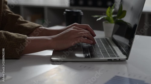 Woman Typing on Laptop Keyboard in Office Setting with Plant and Minimalist Desk