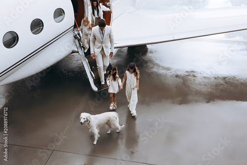 High-angle view of a family with a dog boarding a private plane on a wet tarmac of a private airport for a family vacation