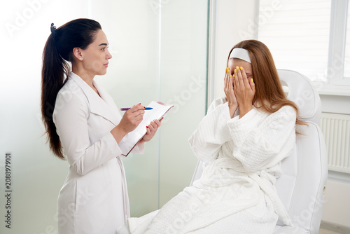 Schilderij op canvas Cosmetologist consulting scared female patient and making notes during medical a