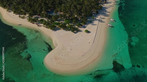 Aerial drone flight flying forward toward Tangkahan Island, Balabac, Palawan, Philippines. Straight tracking shot over transparent turquoise ocean reveals tropical hook-shaped sandbar.