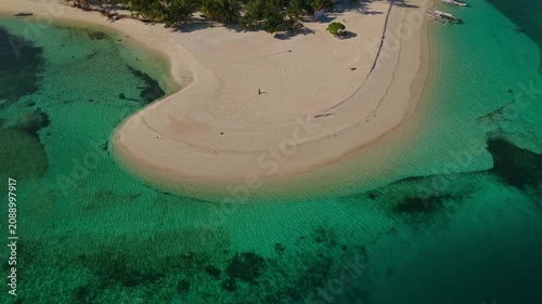 Aerial vertical descent with gimbal tilt up over Tangkahan Island, Balabac, Palawan, Philippines. Drone drops down over turquoise reef while tilting up to reveal tropical hook sandbar.