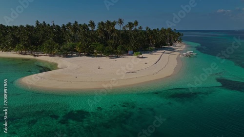 Aerial tracking orbit of Tangkahan Island moving left to right, Balabac, Palawan, Philippines. Panoramic drone shot reveals tropical hook-shaped sandbar, palm trees, and turquoise reef.