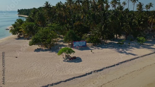 Aerial backward reveal flight of Tangkahan Island, Balabac, Palawan, Philippines. Pull away drone tracking shot showcases tropical palm trees, a unique hook-shaped white sandbar, and turquoise ocean.