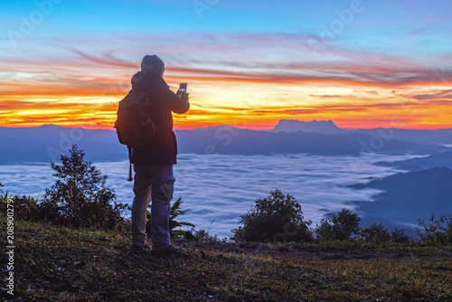 Male Hiker with backpack using smartphone taking photos mountains landscape. Sharing travel lifestyle and adventure vacations. Use outdoor modern technology