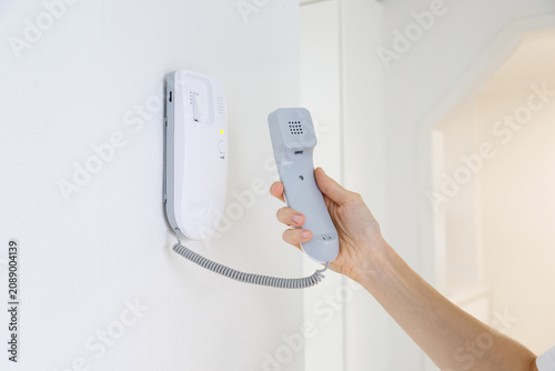 Obraz na płótnie Close up of a hand holding a home intercom handset while responding to a visitor