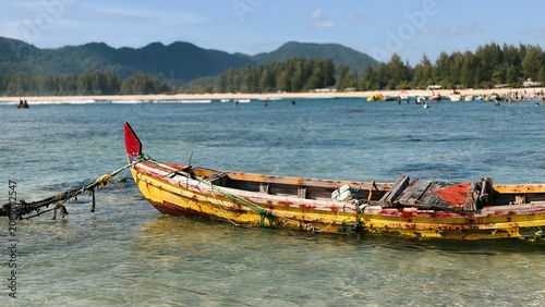 Fotografie Rustic wooden boat anchored in clear turquoise water by a tropical beach with lu