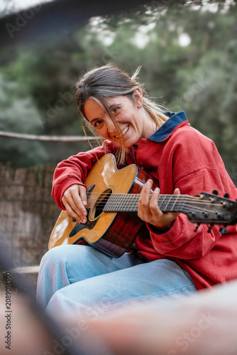 Woman laughing playing acoustic guitar outdoors