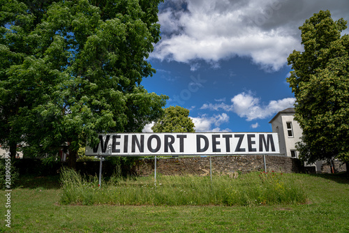 wo dieses kunstvoll geschnitzte Ortsschild wie ein stiller Wächter am Wegesrand steht. Das warme Holz erzählt von Weinbergen, Tradition und Menschen, die seit Generationen mit der Landschaft leben.