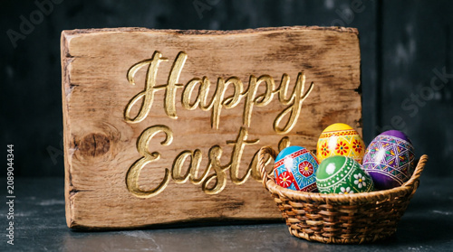 Rustic Happy Easter sign with pastel decorated eggs in wicker basket celebrating spring joy.