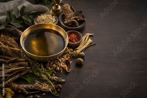 Ayurvedic herbal oil in a brass bowl with organic herbs, spices and medicinal roots for spa wellness therapy