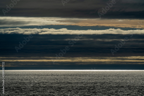 Tableau sur toile Layered stratus clouds glowing above open sea with light breaking through horizo