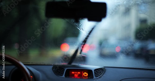 Point of view car drive in city on a rainy day with active windshield wipers and blurry bokeh street lights