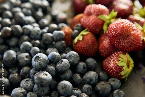 Photos Macro close-up of fresh ripe blueberries and red strawberries on dark textured s