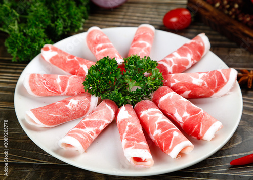 Premium Raw Beef Rolls with Parsley Garnish on White Plate for Fondue and Hot Pot Cooking