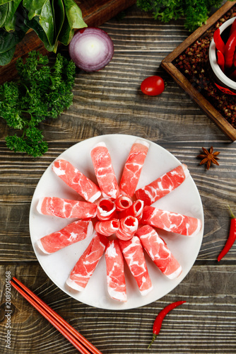 Raw Marbled Beef Slices Arranged on Plate with Fresh Herbs and Spices for Gourmet Cooking