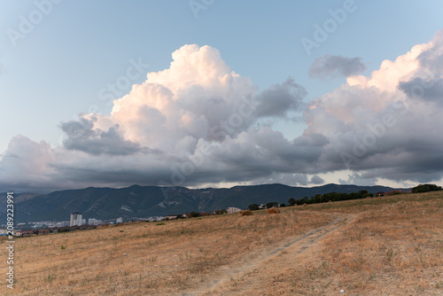 cloud hanging over a dry rural road, hay bales and distant mountains