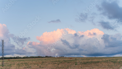 Panoramic dry rural field under pastel sunset clouds.