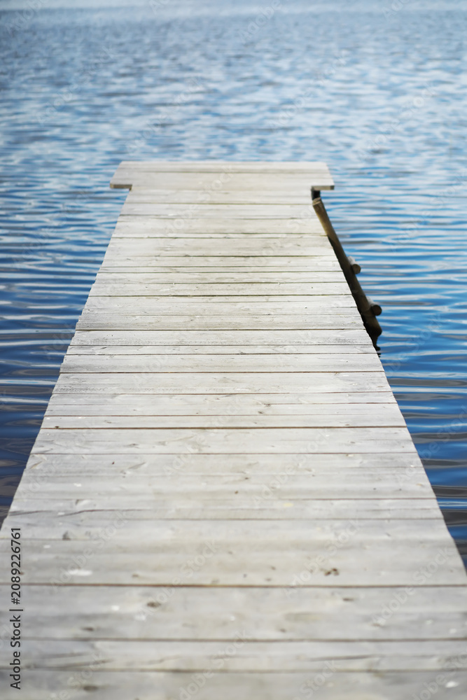 Fototapeta premium Serene Wooden Dock Extending Into Calm Blue Lake Waters on a Sunny Day