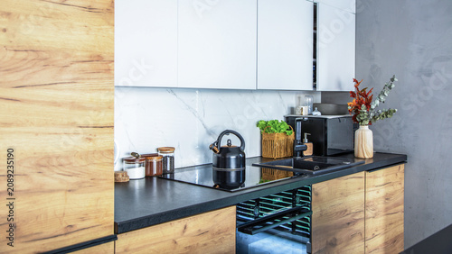 Cozy loft style kitchen design featuring elegant white and wood textured cabinets, built-in appliances, a black kettle, and stylish decor.