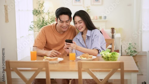 Young Couple Enjoys Breakfast Together While Sharing Laughs and Looking at a Smartphone