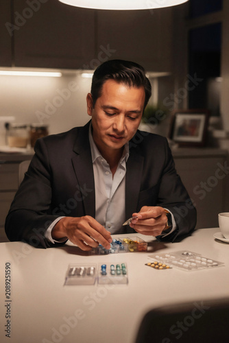 Professional Man Sorting Medication in Pill Organizer Late at Night
