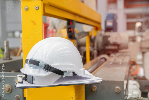 White safety helmet and clipboard placed on industrial machine in bright factory environment conveying focus and responsibility in workplace safety