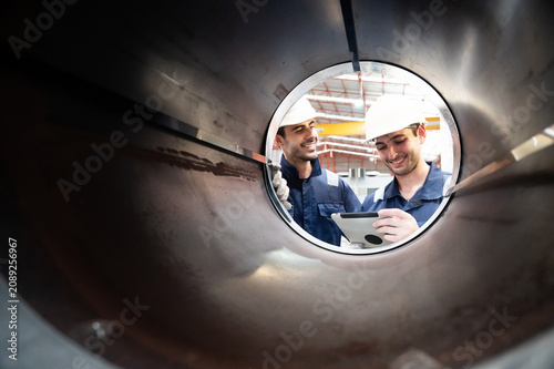 Bild auf Leinwand Two factory workers in safety helmet inspect large metal pipe using tablet, smil