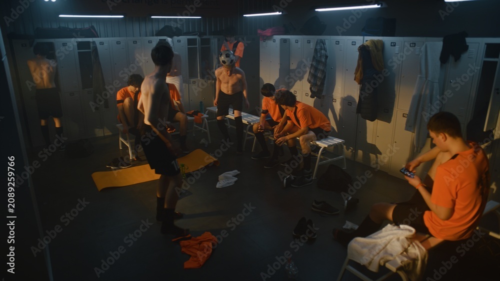 Obraz premium Youth Football Players Relaxing in Locker Room after Training Session. Teammates Change Clothes, Prepare For Shower, Chat About Practice, One Player Juggles Soccer Ball. Atmosphere of Amateur Sports.