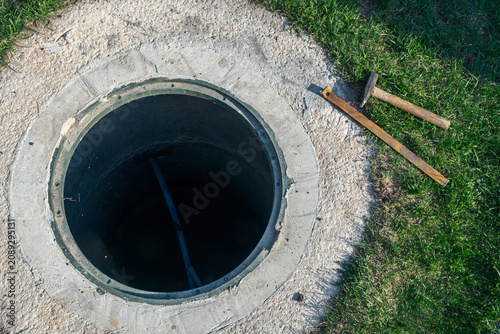 Open manhole repair process on green lawn backyard sewer line maintenance with hammer tool underground utilities infrastructure
