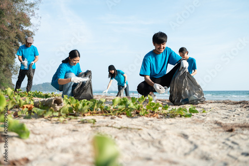 Group of active Asian volunteers cleaning up plastic waste and garbage on the beach together, focusing on environmental conservation and community teamwork.