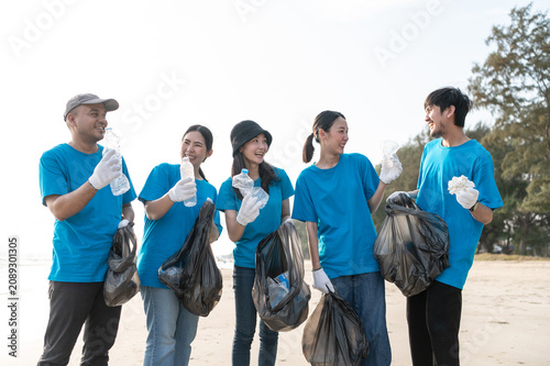 Group of active Asian volunteers cleaning up plastic waste and garbage on the beach together, focusing on environmental conservation and community teamwork.