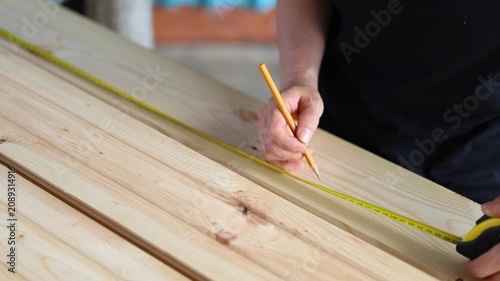 Close-up of a craftswoman marking wood with a pencil in a workshop. Female carpenter's hands measuring a wooden plank with a yellow tape measure. Slow motion 4K footage.