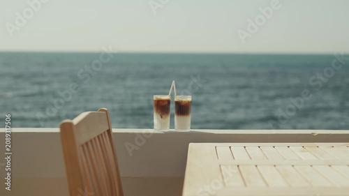 Two iced coffees sit on a table overlooking a calm blue ocean view
