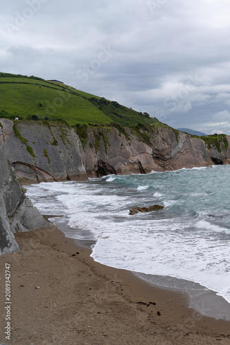 Dramatic geological formations meet the ocean waves on a sandy beach in Zarautz, Basque Country