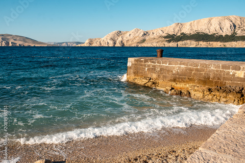 Foto Stone pier and turquoise sea waves gently lapping on a pebble beach
