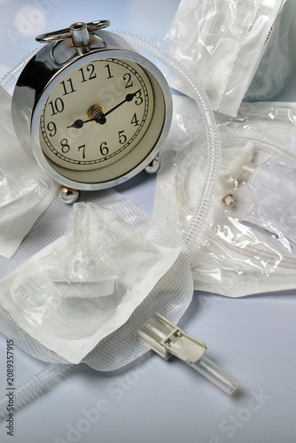 an old alarm clock, a urine bag, and several male silicone catheters