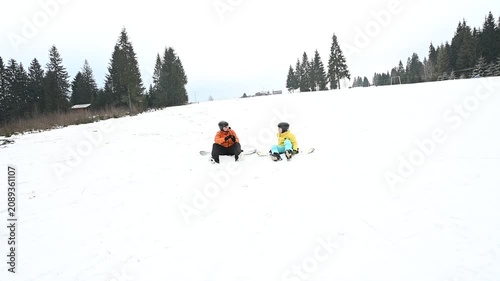 Two snowboarders rest on a snow-covered slope amidst a backdrop of evergreen trees. A tranquil winter scene.