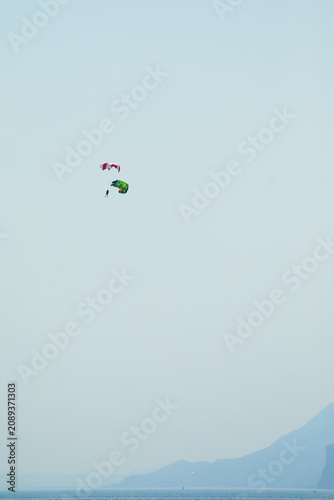 Paraglider pilot performing a safety training exercise with an open reserve parachute, descending safely toward the water during an emergency procedure simulation.