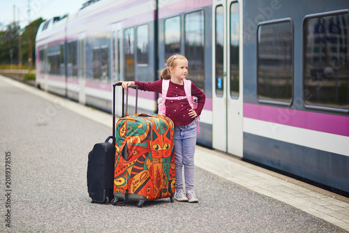 Happy young girl standing with colorful suitcases on a train platform in Finland, ready for travel and family trip by rail