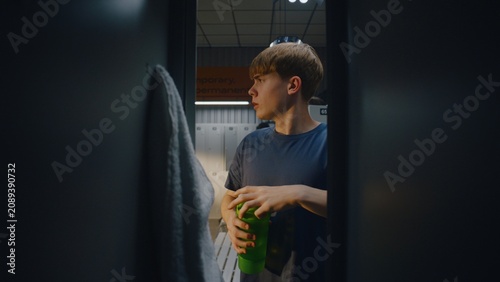 Inside Gym Locker Young Male Athlete Opens Door. Boys Places Black Sports Bag Inside Compartment, Grabs Water Bottle, and Takes Sip Before Heading Out. Realistic Athletic Preparation Routine.