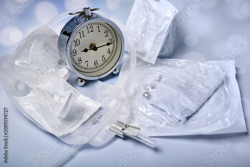 An old-style alarm clock, several male silicone catheters and a urine collection bag on the table