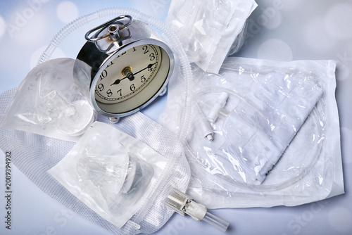 There are several silicone catheters and a urine collection bag on the table, and an alarm clock stands nearby.