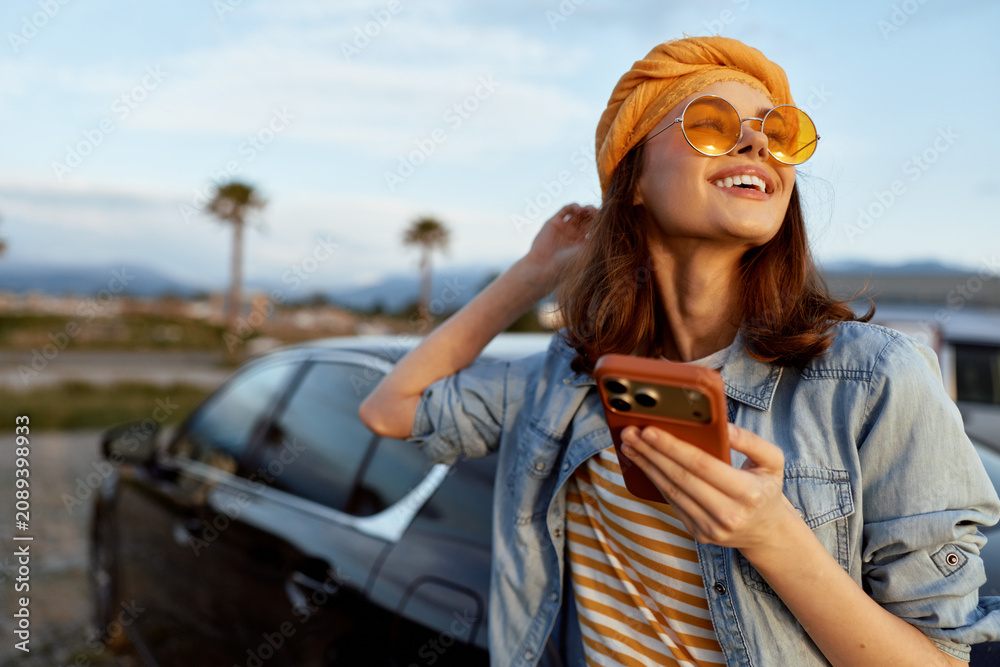 Naklejka premium woman lifestyle outdoor sunny smiling smartphone denim jacket fashion casual portrait mood as she relaxes beside a car enjoying a bright day and free spirited vibe