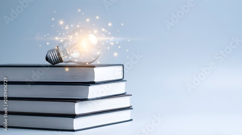 Glowing light bulb emits sparks of energy resting on a stack of hardcover books, creating a concept of knowledge and learning against a white background
