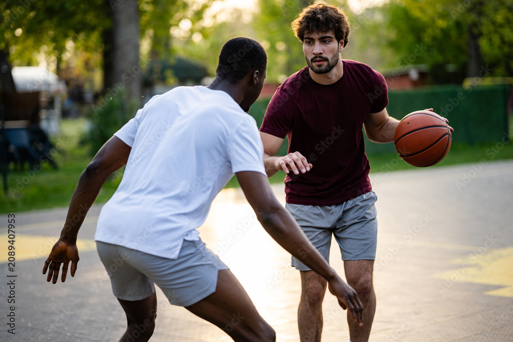 Fototapeta premium Young men playing competitive street basketball outdoors