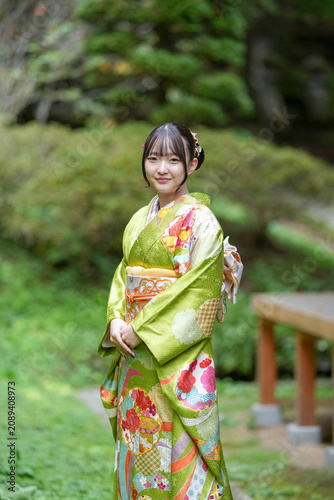A woman in a green kimono poses in a park. Concept of elegance and grace, as the woman stands tall and confident in her traditional attire